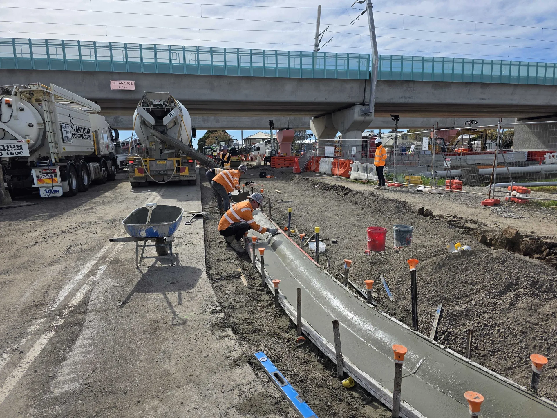 Workers hand-finishing a concrete kerb within a rail-adjacent external works site.