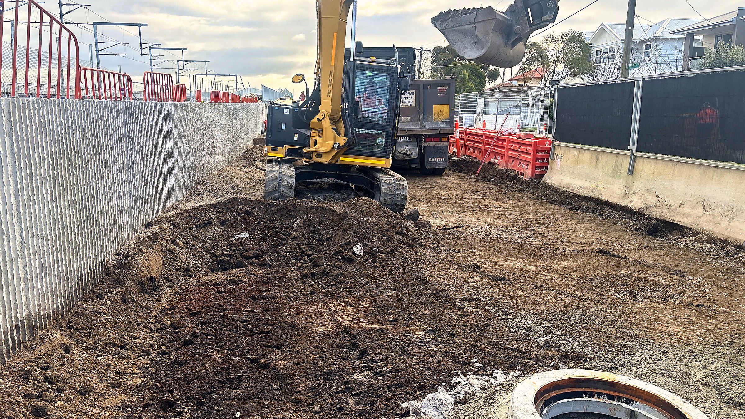 Crew and plant working within a barricaded corridor beside live infrastructure.
