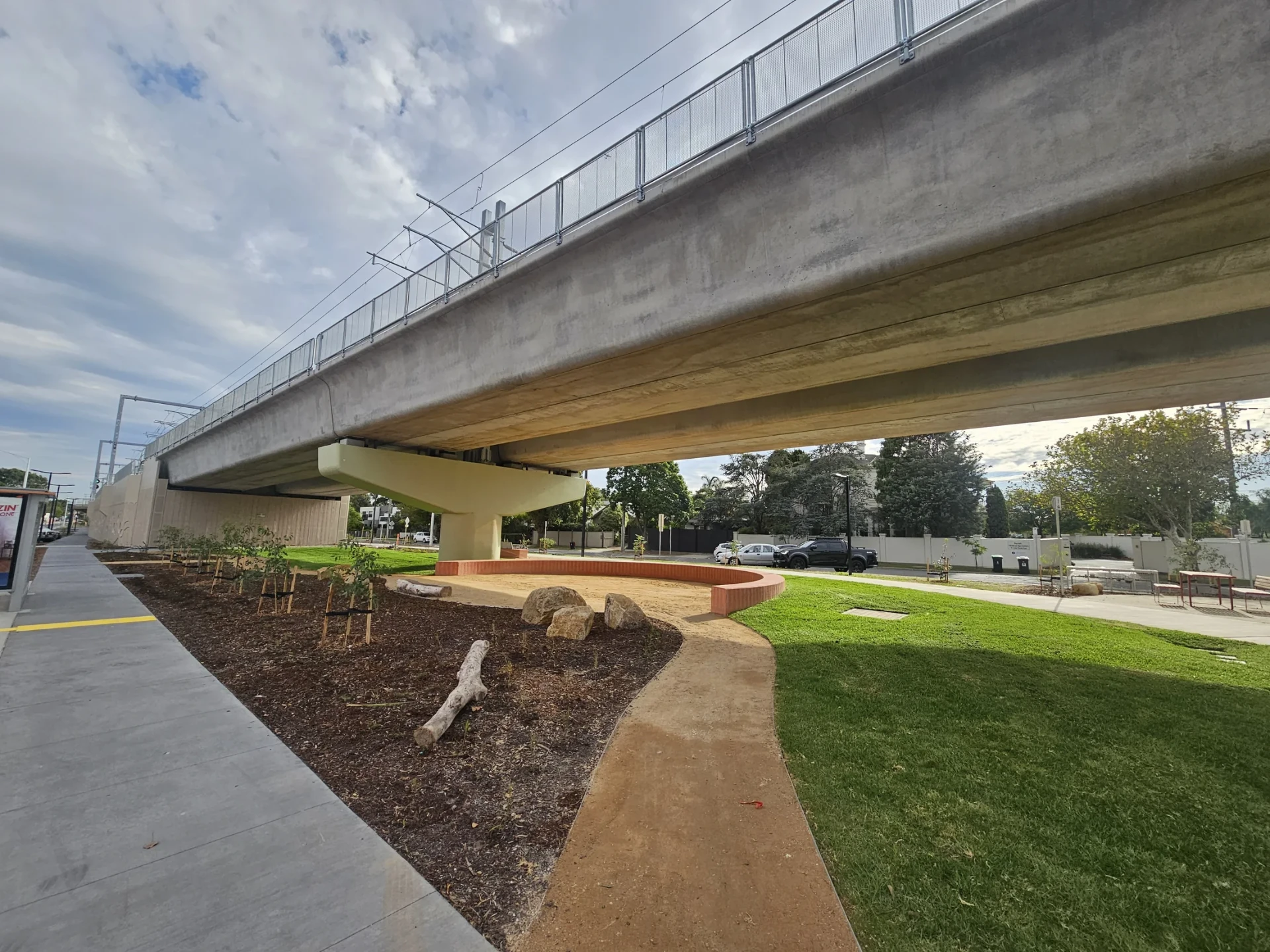 Completed public-realm paths, garden beds, boulders and planting beside transport infrastructure.
