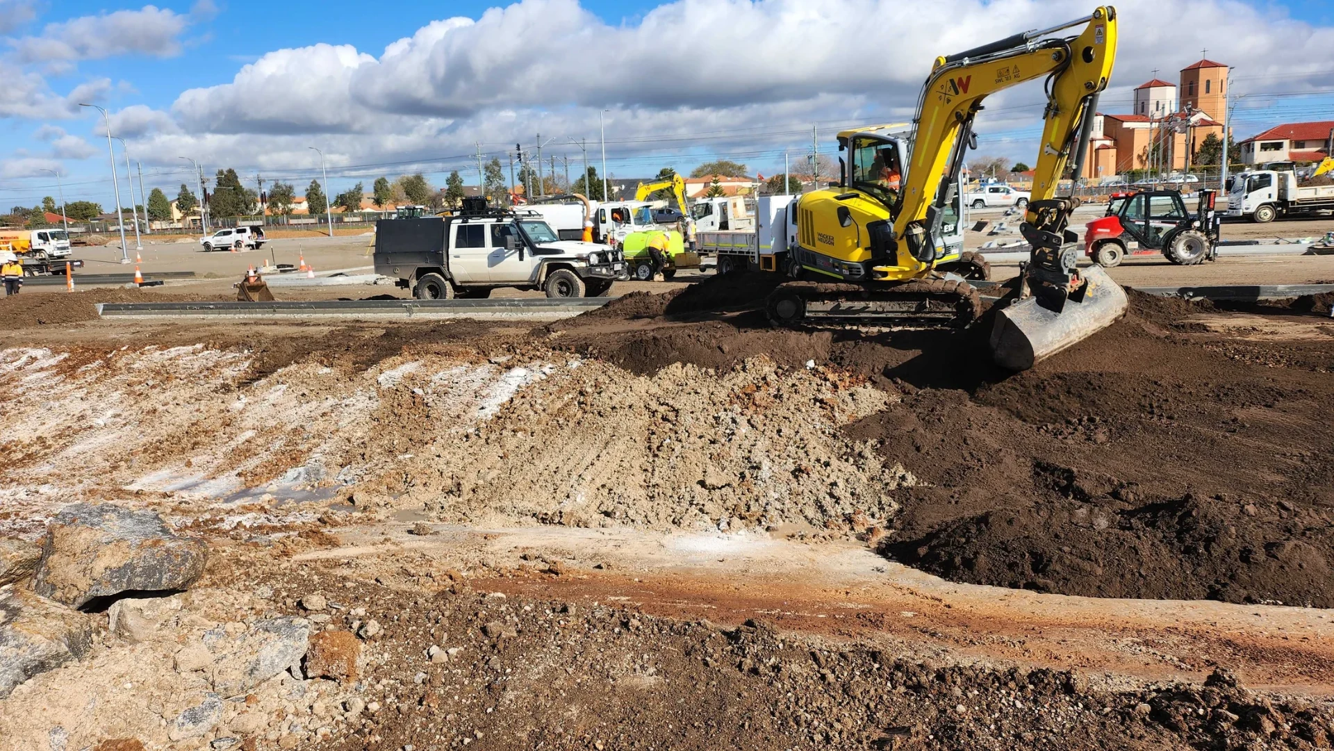 Excavator shaping a prepared external works area beside newly constructed kerb.